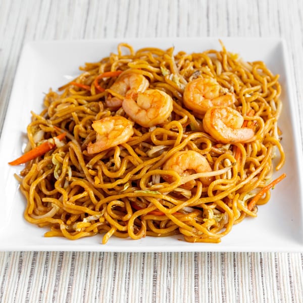 Shrimp lo mein with noodles, carrots, and cabbage on a white rectangular plate.