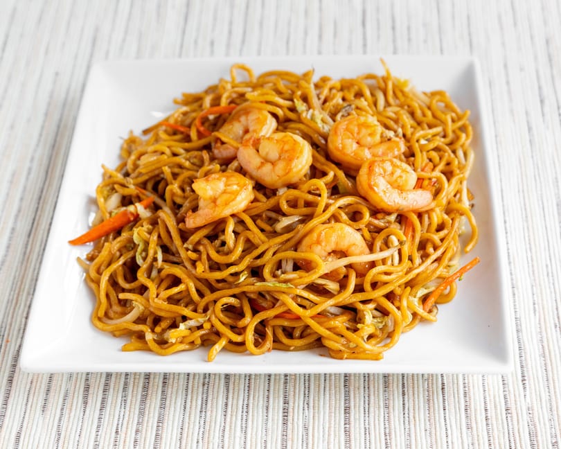 Shrimp lo mein with noodles, carrots, and cabbage on a white rectangular plate.