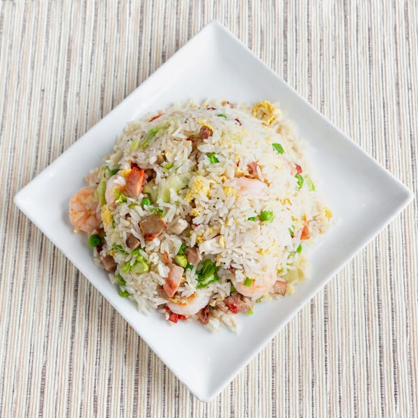 A white square plate filled with fried rice, shrimp, pork, egg, and green peas.