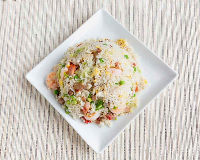 A white square plate filled with fried rice, shrimp, pork, egg, and green peas.