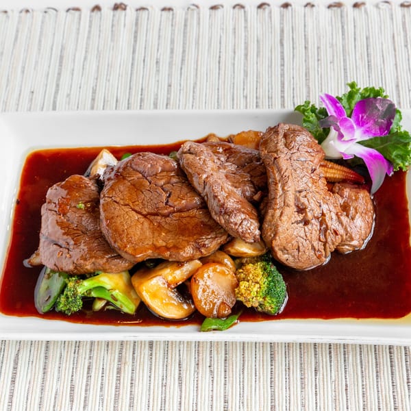 Beef medallions with broccoli, mushrooms, baby corn, and a purple orchid garnish in a rich brown sauce.