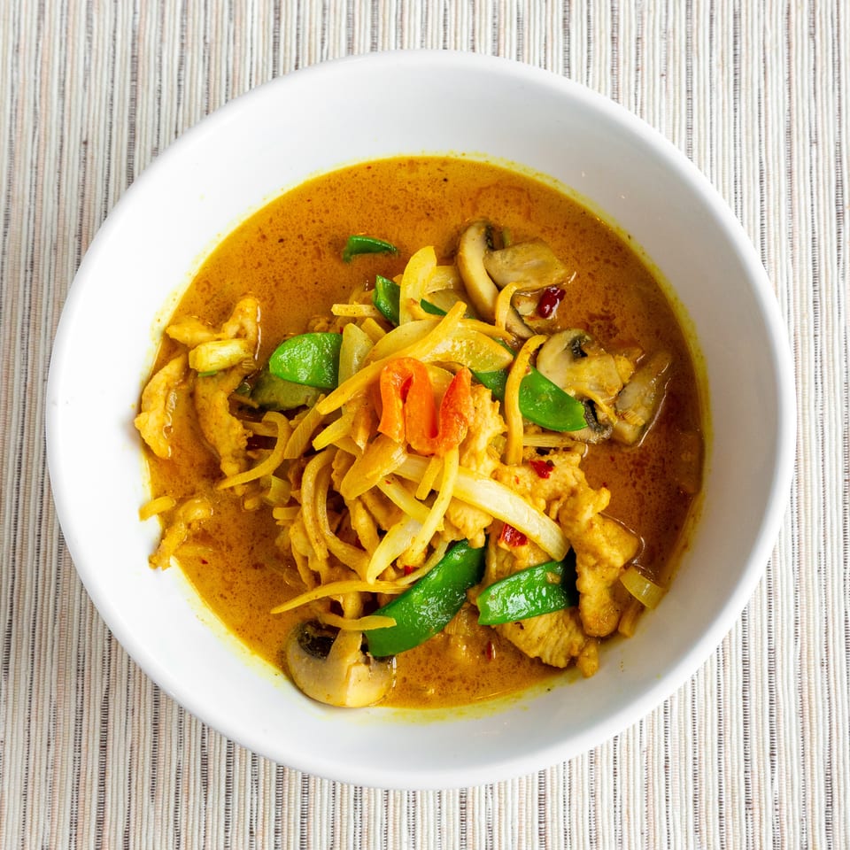 A white bowl filled with yellow curry, chicken, mushrooms, onions, and green peppers.