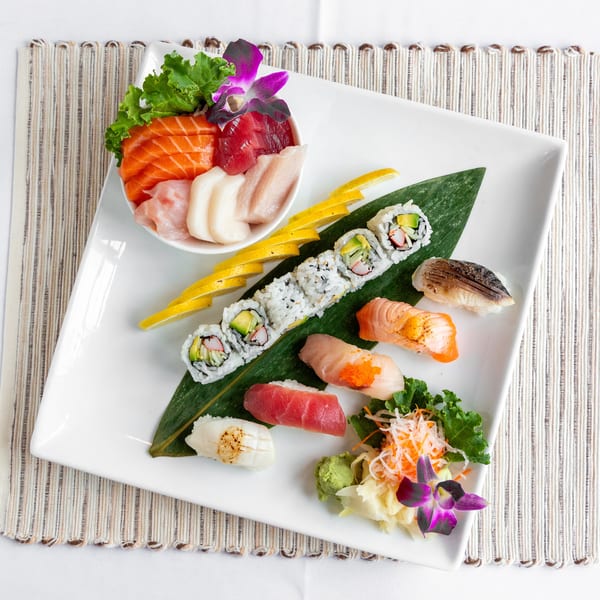 A white rectangular plate holds a variety of sushi, sashimi, and rolls, garnished with lemon and orchids.