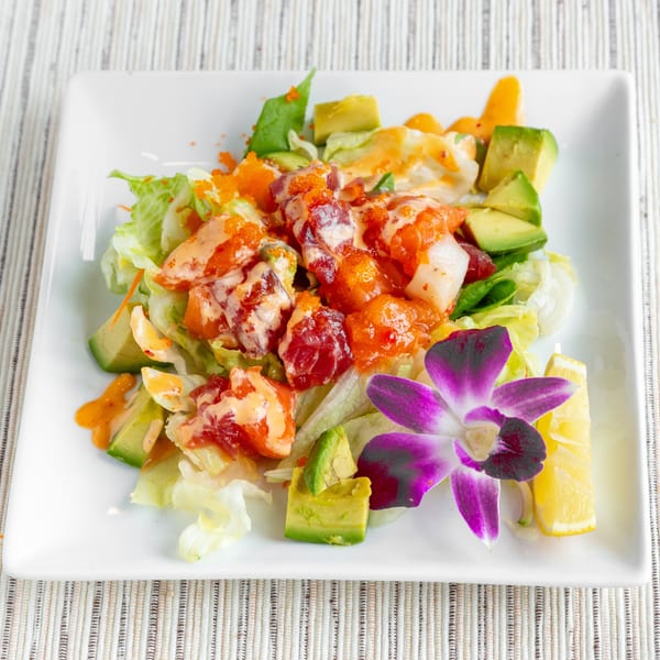 Colorful poke salad with avocado, lettuce, fish, and roe, garnished with a purple orchid and lemon.