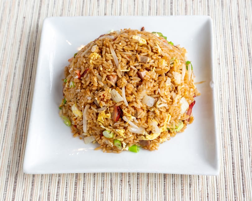 A large serving of fried rice with egg, pork, and vegetables on a white square plate.