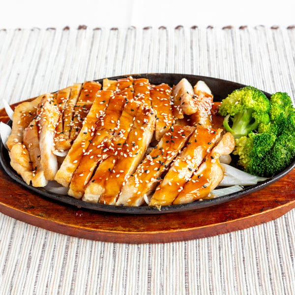 Teriyaki chicken with sesame seeds and broccoli on a sizzling plate with onions.