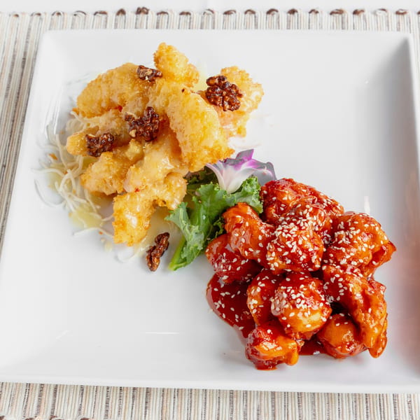 A white rectangular plate with two distinct dishes: honey walnut shrimp and sesame chicken.