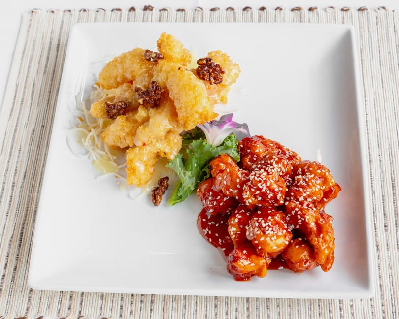 A white rectangular plate with two distinct dishes: honey walnut shrimp and sesame chicken.