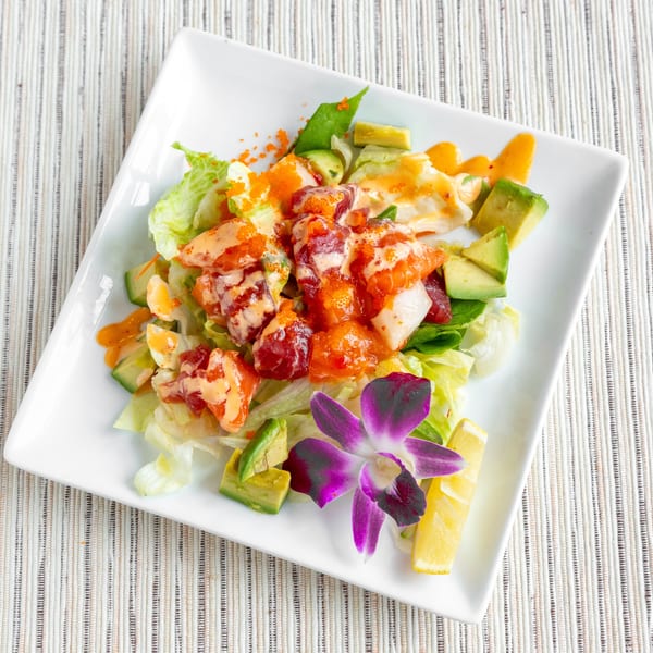 A vibrant seafood salad with lettuce, avocado, and a purple orchid garnish on a white plate.