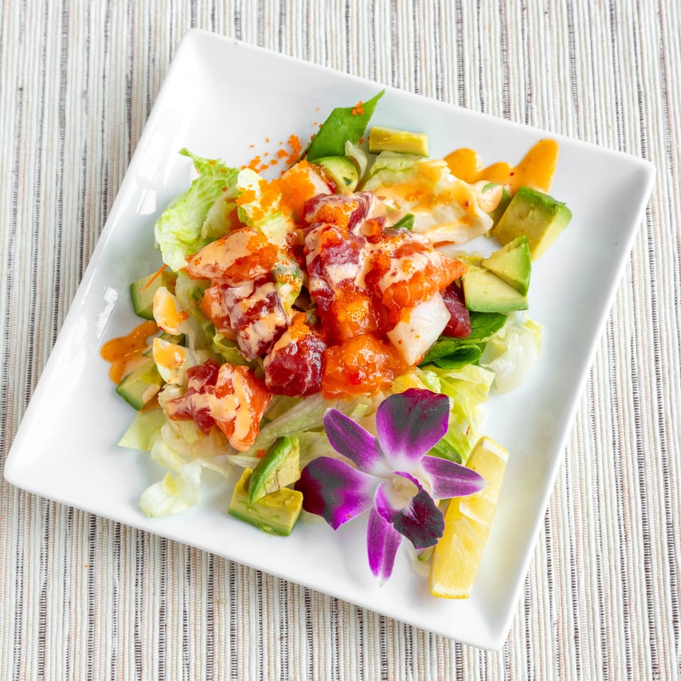 A vibrant seafood salad with lettuce, avocado, and a purple orchid garnish on a white plate.