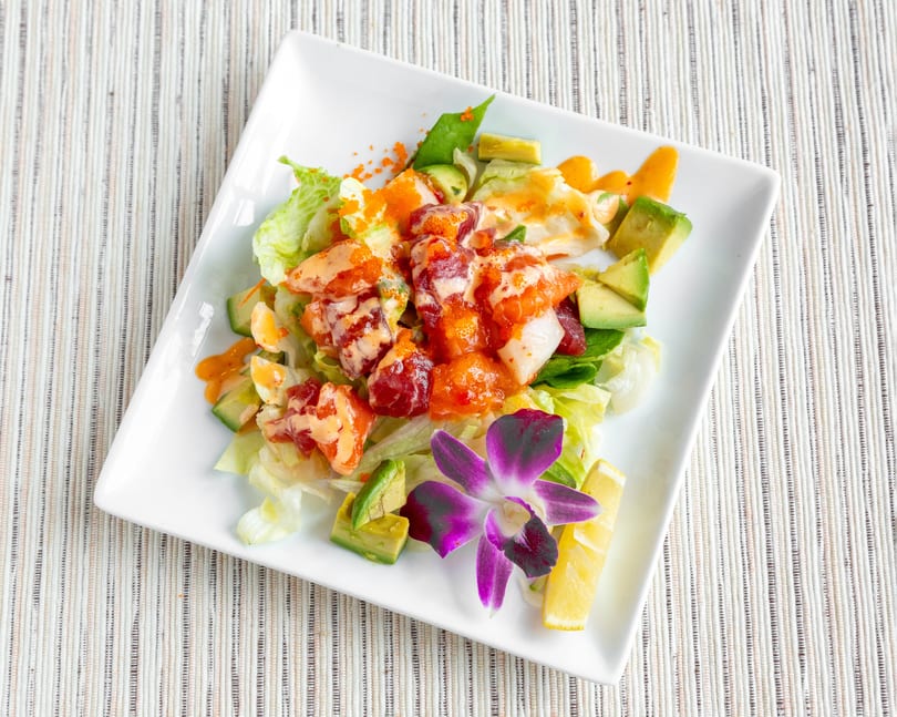 A vibrant seafood salad with lettuce, avocado, and a purple orchid garnish on a white plate.