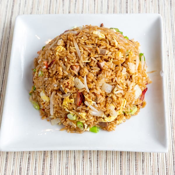 A large serving of fried rice with egg, pork, and vegetables on a white square plate.