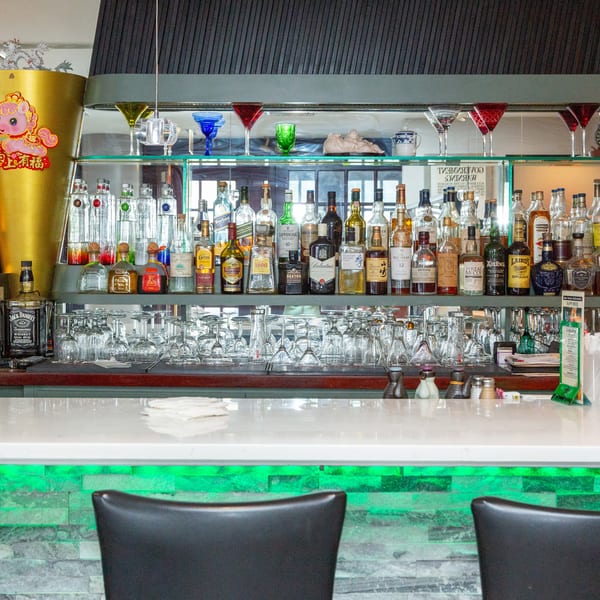 A well-stocked bar with various liquor bottles, glassware, and a white countertop with green lighting.