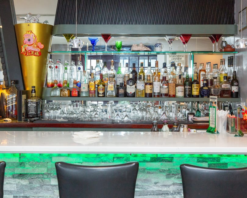 A well-stocked bar with various liquor bottles, glassware, and a white countertop with green lighting.