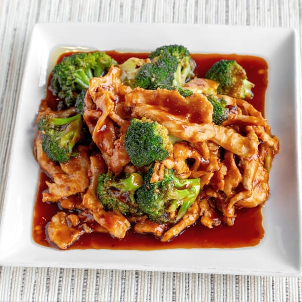 Chicken and broccoli stir-fry in a rich brown sauce, served on a white rectangular plate.