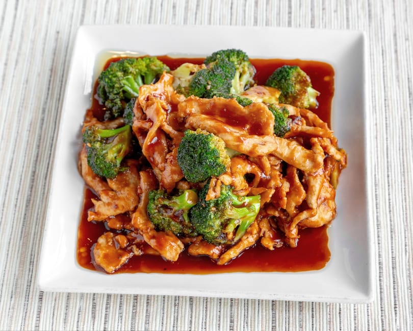 Chicken and broccoli stir-fry in a rich brown sauce, served on a white rectangular plate.